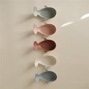 Whale-shaped bath stackers in pastel shades of green, pink, white, and blue, arranged vertically against a light background.