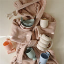Mushie Whale Bath Stackers in various colors displayed among a pink towel, showcasing stacking cups and a whale design.