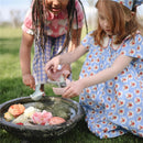 Two children play with Mushie Whale Bath Stackers, pouring water into a basin filled with colorful flowers.