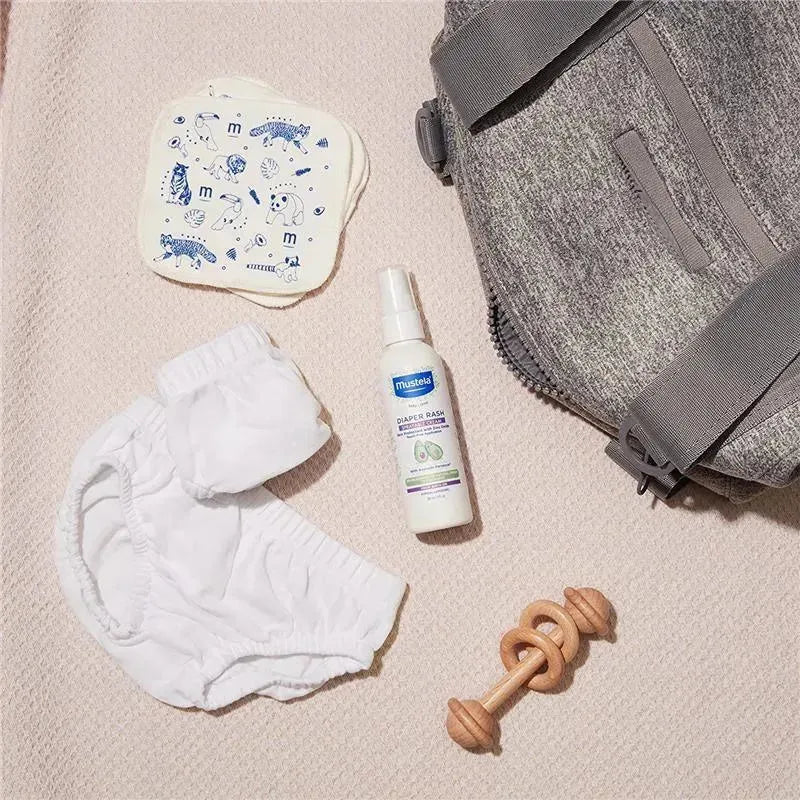 Mustela 6Ct reusable eco-wipes, diaper cream, white cloth diapers, a wooden toy, and a gray diaper bag on a light surface.