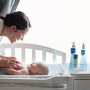 Mother smiling at her baby in a crib, with Mustela Hair Styler & Skin Freshener products displayed on a nearby surface.