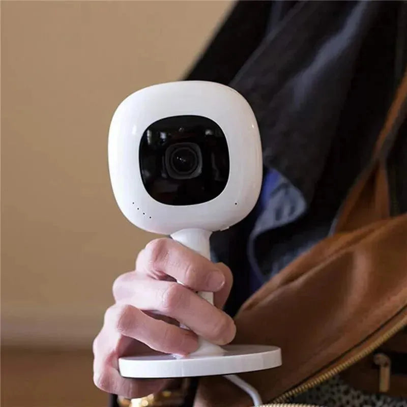 Nanit Flex Multi-Stand baby monitor accessory held in a hand, featuring a white body and black camera lens.