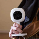 Nanit Flex Multi-Stand baby monitor accessory held in a hand, featuring a white body and black camera lens.