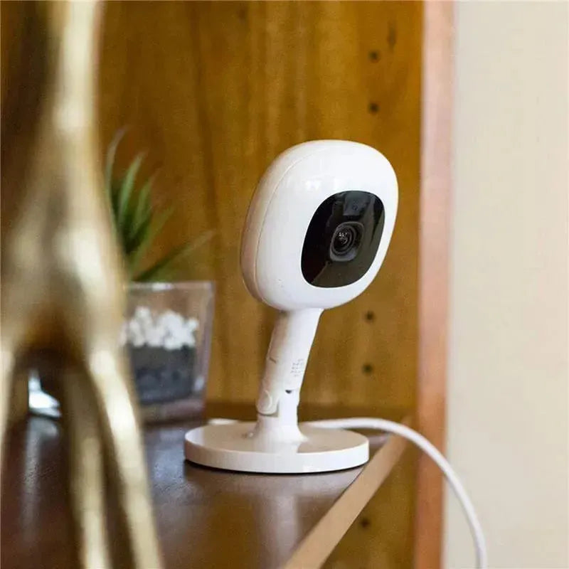 Nanit Flex Multi-Stand Baby Monitor positioned on a shelf, featuring a round base and a sleek design with a visible camera lens.