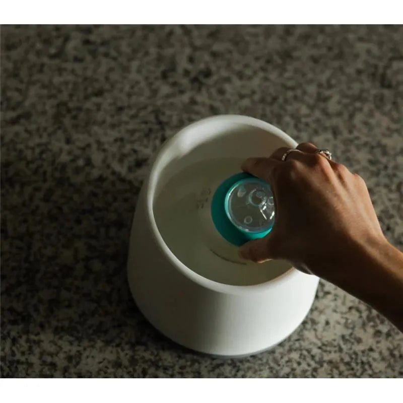 Nanobebe teal breastmilk bottle warming bowl with a hand placing a bottle into warm water.