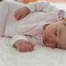 A sleeping baby wearing a pink Nested Bean Medium Zen Sack Classic, with a stitched bear design, resting on a soft blanket.