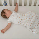 A sleeping baby in a white onesie with a cute face design, wearing the Nested Bean Zen Sack Classic in Monogram Amber.