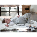 Baby wearing a Nested Bean Zen Sack in solid gray, lying on a fluffy white rug, with a playful expression.
