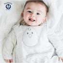 Smiling baby in a Stardust Grey Nested Bean Zen Sack, featuring a cute bird design on the front, lying on a white blanket.