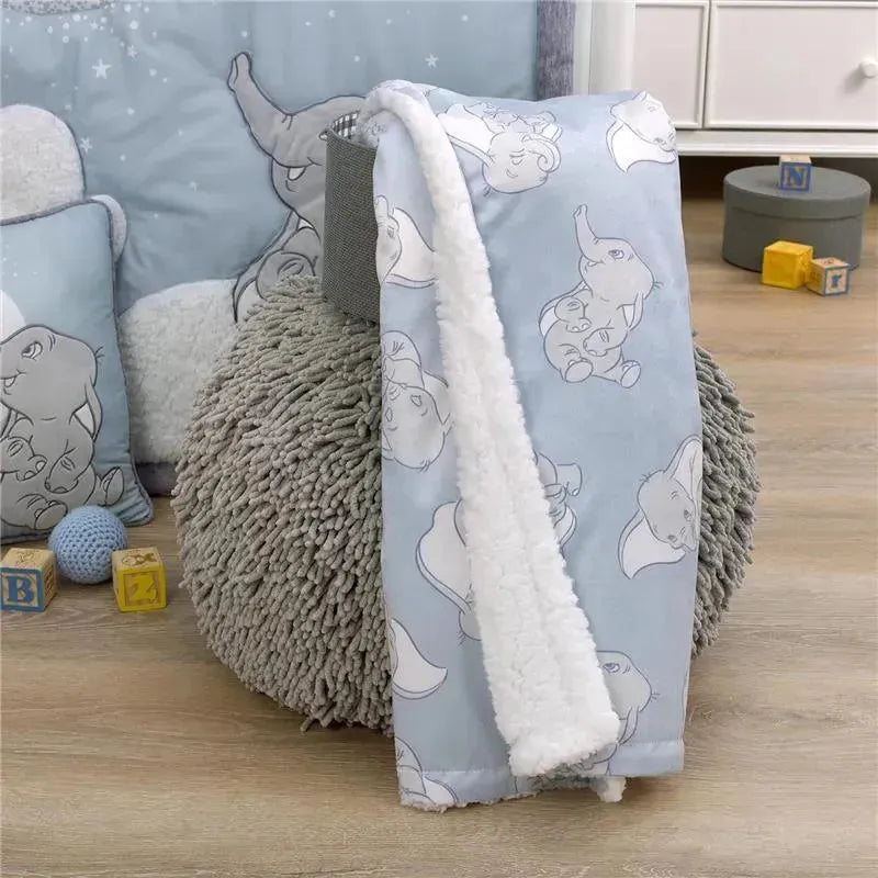 Soft, light blue baby blanket featuring Dumbo illustrations, with a plush white sherpa lining, displayed on a textured pouf.