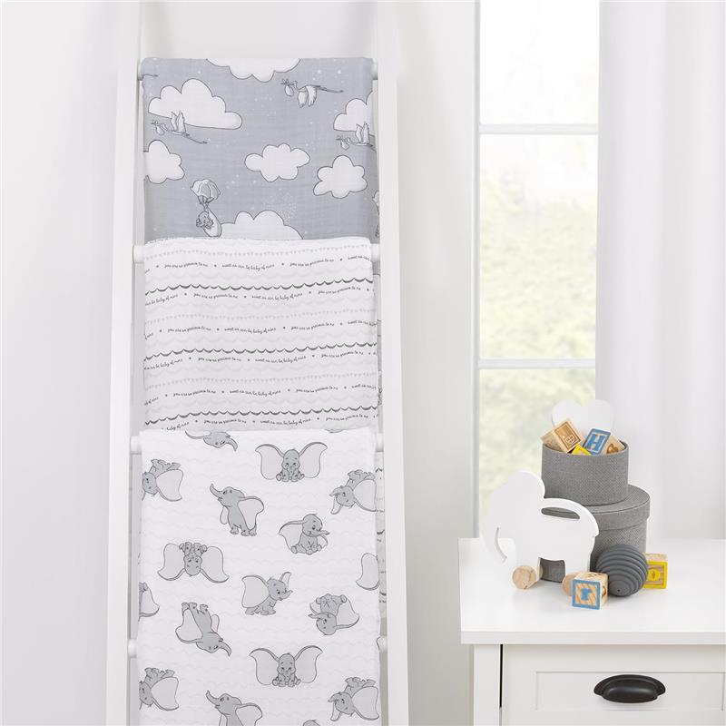 Three Nojo Dumbo printed muslin swaddles displayed on a white rack, featuring Dumbo designs and soft gray tones.