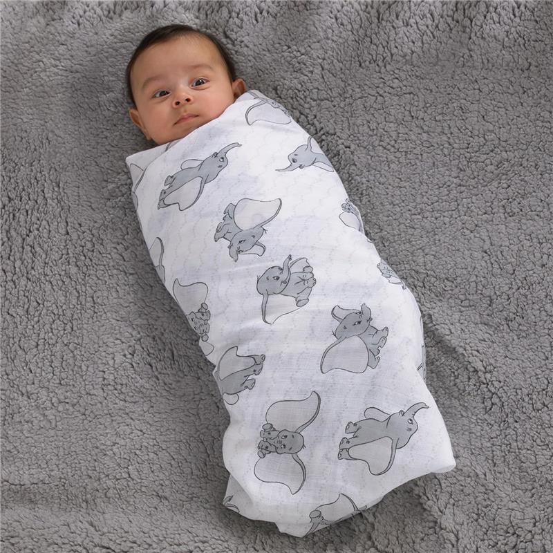 Muslin swaddle with Dumbo prints, wrapping a baby, on a soft gray blanket.