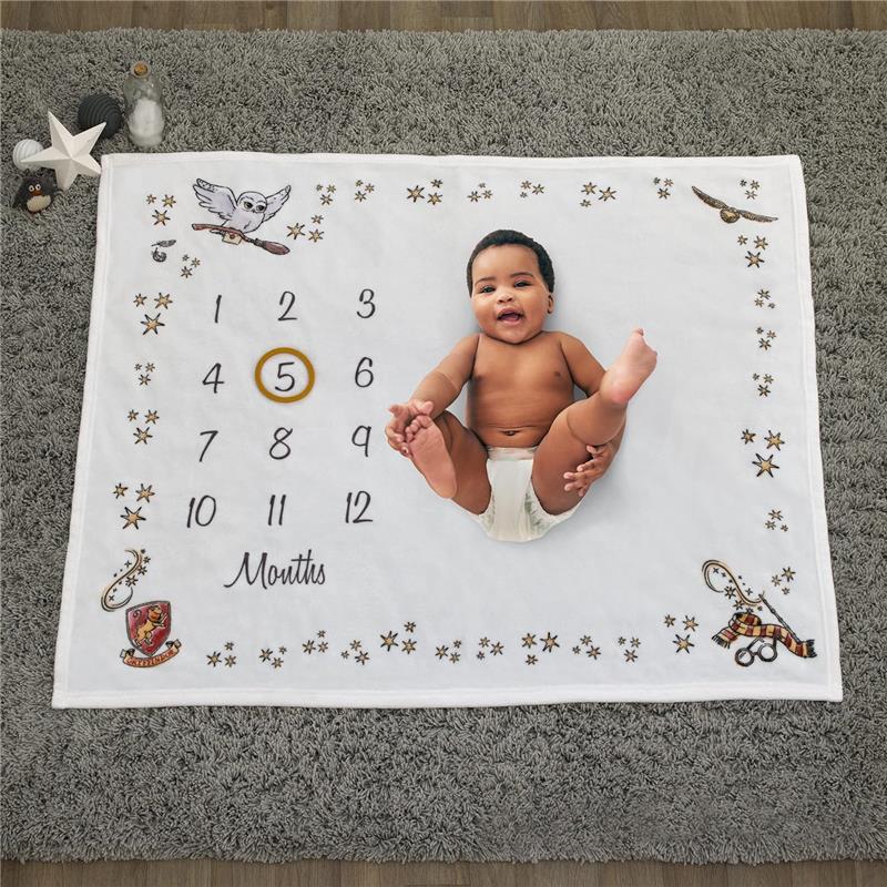 Milestone blanket featuring a baby lying on a white fabric with a numbered calendar from 1 to 12 and whimsical Harry Potter-themed decorations.