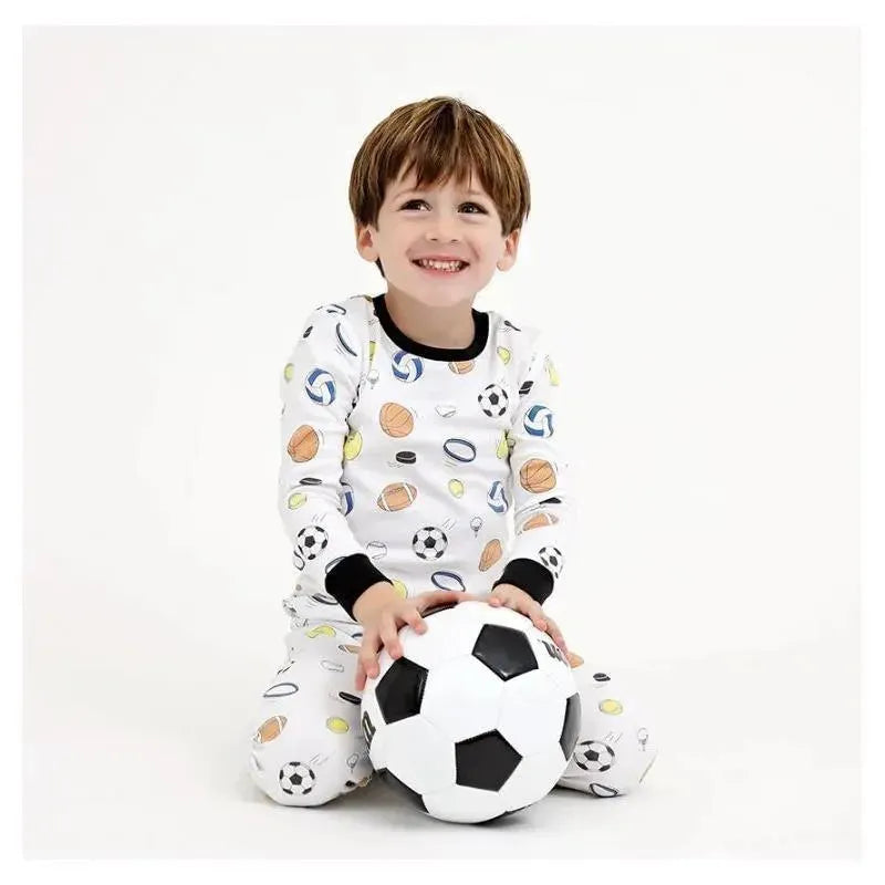 Boy wearing a white pajama set with sports patterns, sitting and holding a black and white soccer ball, smiling.