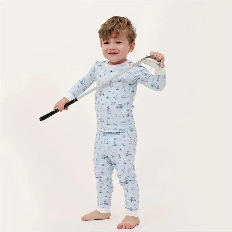 Baby boy in a blue pajama set with golf-themed patterns, holding a golf club and smiling.