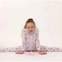 Baby girl wears a long-sleeve pajama set with a cake print, smiling while sitting with legs extended on a white background.