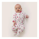 Baby girl in a zipped footie covered in cosmetics patterns, smiling and posing against a light background.