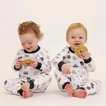 Two toddlers in cookie-patterned long sleeve pajamas sit on a light background, each holding a cookie.