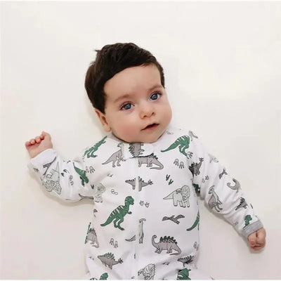 Baby wearing a Noomie Dinosaurs Zipper Footie with various dinosaur prints, lying on a plain background.