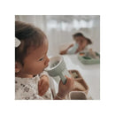 Child drinking from a light green Nouka All Around Cup, with a white interior, sitting at a table with food.