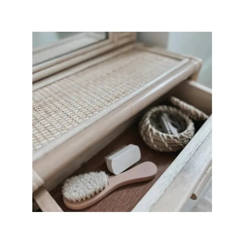 Baby nail clipper in soft blush, alongside a wooden brush and other baby care tools, inside a drawer.