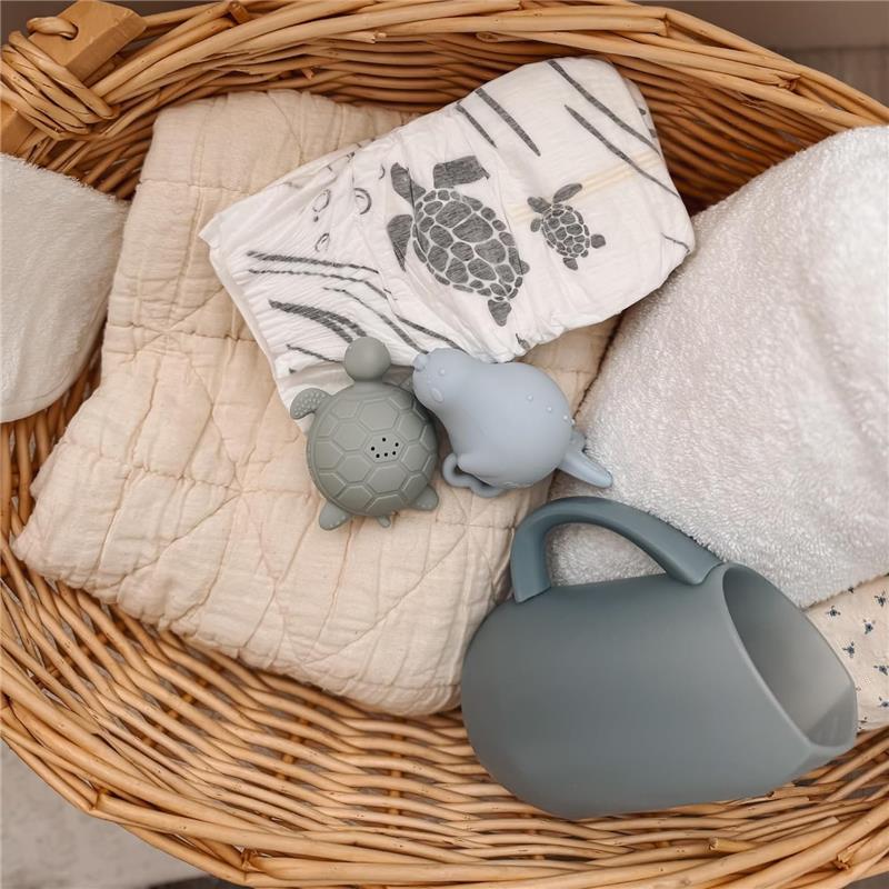 Nouka Bath Rinse Jug in Soft Blush next to grey turtle and seal-shaped bath toys on a soft quilt in a woven basket.