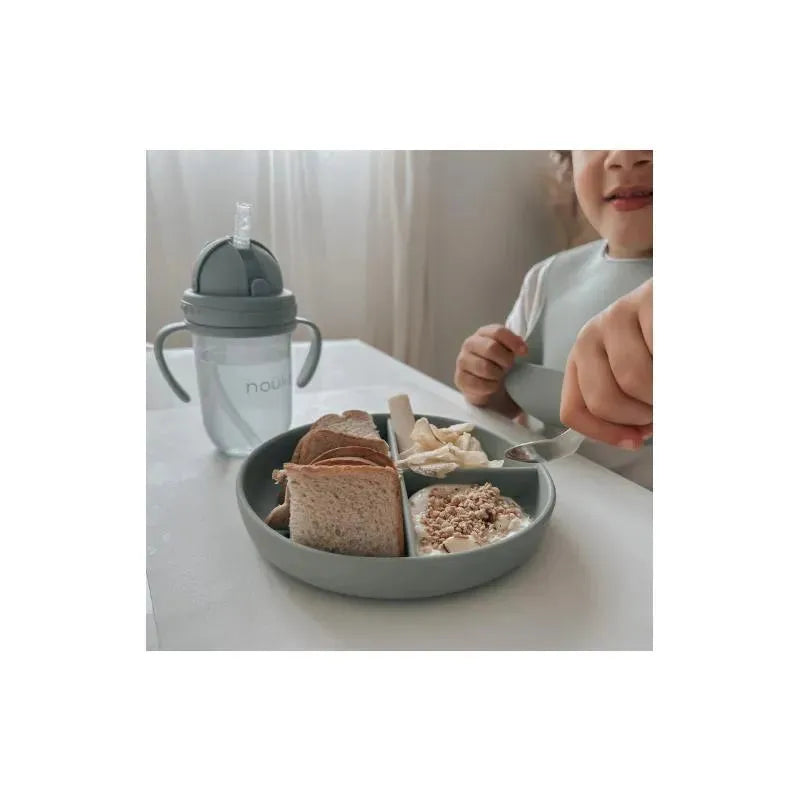 Divided plate with suction containing bread, yogurt, and fruit, with a child holding a spoon and a sippy cup nearby.
