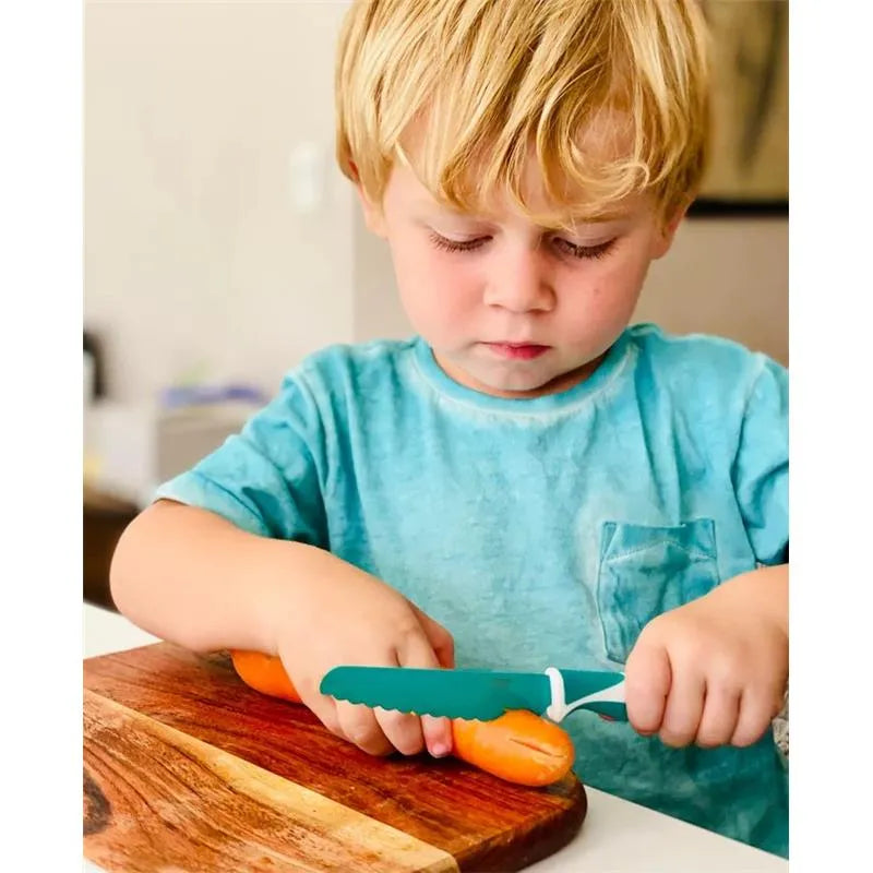 Child using the Nouka Kiddkutter child-safe knife to cut a carrot on a wooden cutting board.