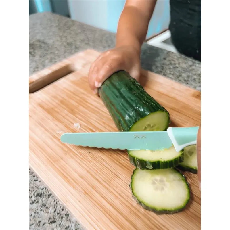 Child using a sea green Kiddkutter knife to slice a cucumber on a wooden cutting board.