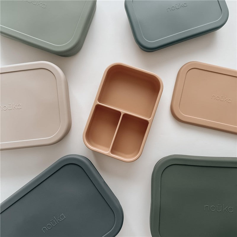 Small silicone-sealed snack box by Nouka, featuring a beige container with three compartments, surrounded by other boxes.
