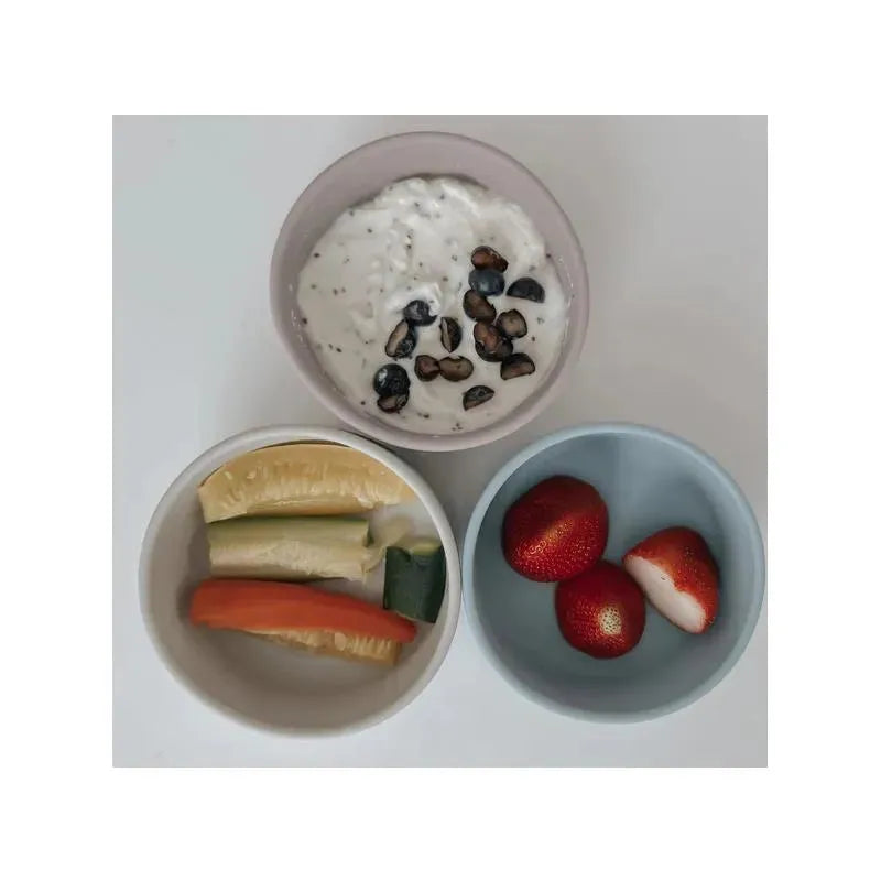 Suction bowls in Lily Blue and pale pink colors contain yogurt with seeds and assorted fruit and vegetable slices.