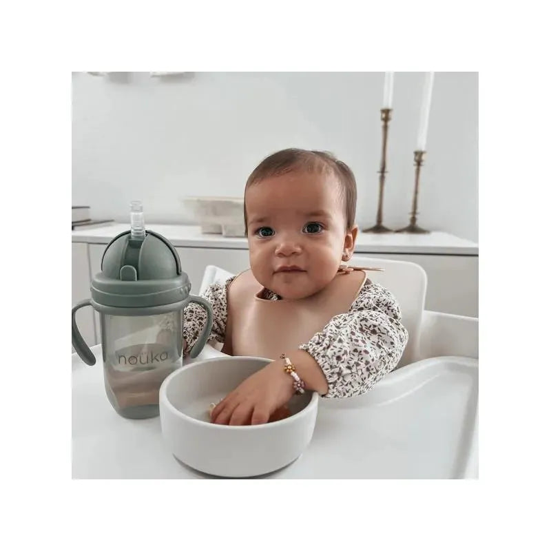A baby in a high chair with a Nouka suction bowl and a sippy cup in Lily Blue, reaching into the bowl.