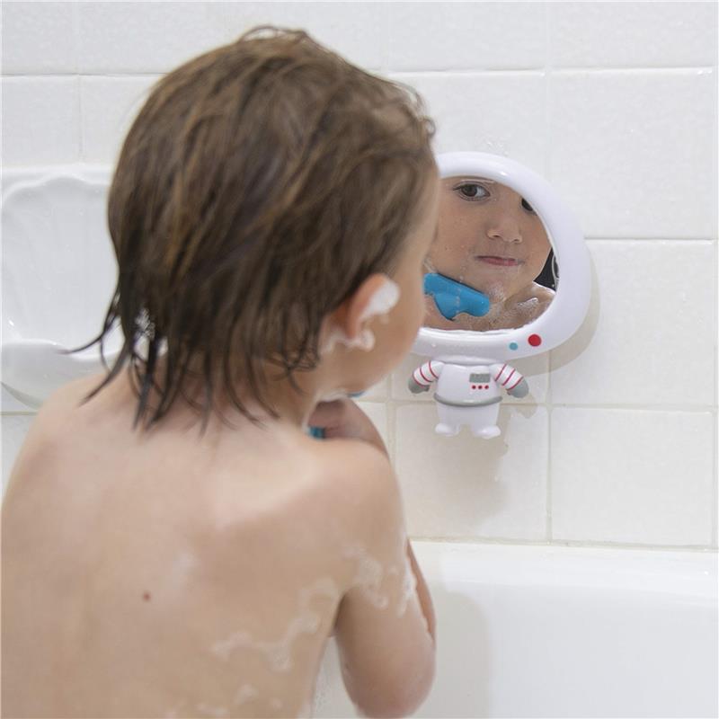 Boy with wet hair looks in a decorative astronaut mirror while playing with a blue toy during bath time.