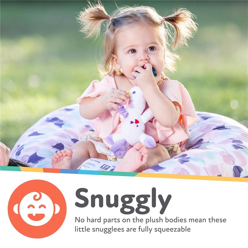 A young child sits on a floral cushion, holding a plush flamingo pacifier while gently sucking on it.