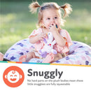 Toddler sitting on a floral cushion, holding a penguin plush pacifier, smiling and enjoying playtime outside.