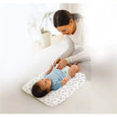 A caregiver gently changes a baby on a Nuby Dr Talbots disposable changing pad, featuring a playful pattern.