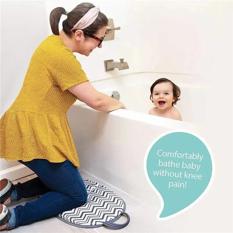 A woman kneels on a Nuby Dr Talbots Folding Knee Pad beside a smiling baby in a bathtub, promoting comfort during bath time.