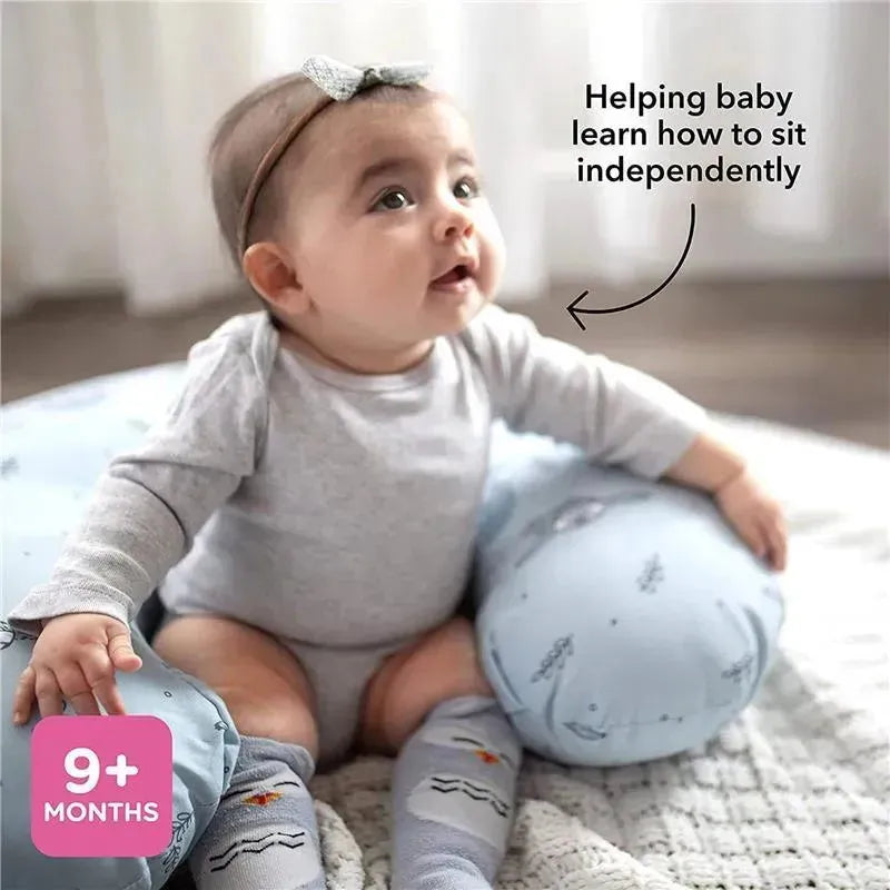 Infant sitting with support pillows featuring a bright floral design, promoting independent sitting at 9+ months.