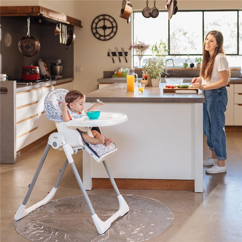 Nuby High Chair Waterproof Floor Mat under a high chair, featuring a child eating from a bowl while an adult prepares food nearby.