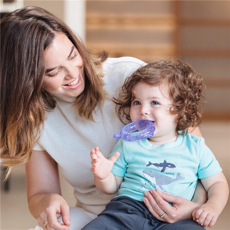 Child smiling while holding a Nuby IcyBite teether, with a woman in a light top engaging with him.