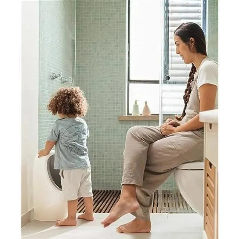 Nuby My Real Urinal Training Toilet with a child practicing urination and a mother sitting nearby in a bathroom setting.