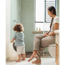 Nuby My Real Urinal Training Toilet with a child practicing urination and a mother sitting nearby in a bathroom setting.