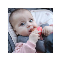 Baby holding a Nuby silicone feeder and post teether, nibbling on food while sitting in a stroller.