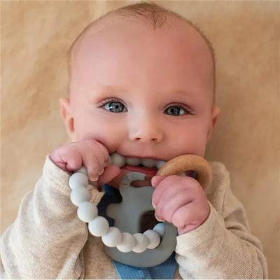Gray silicone and wood teething bracelet held by a smiling baby, featuring round silicone beads and a wooden accent.