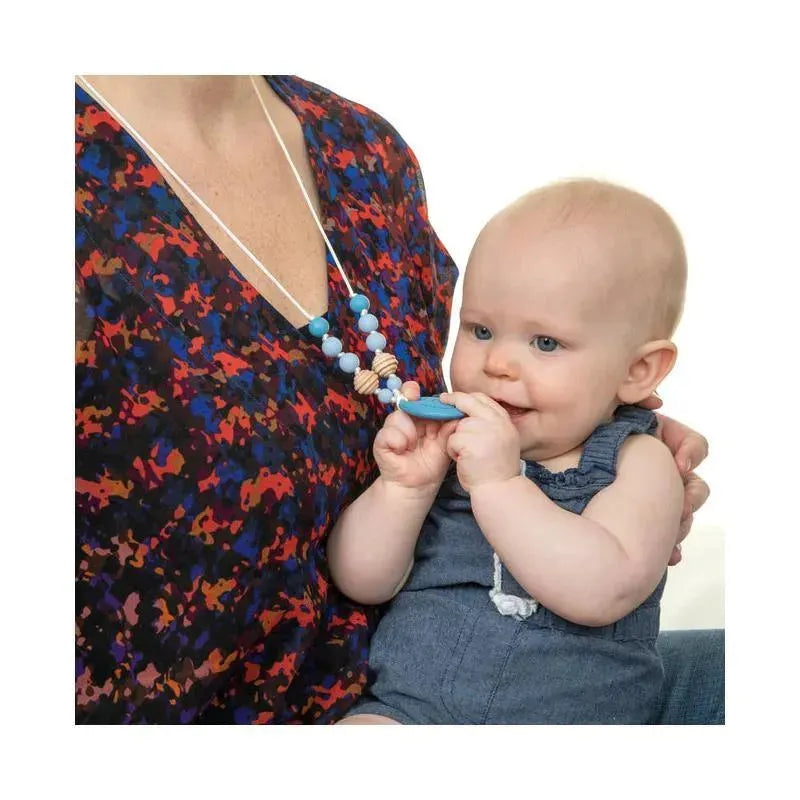 Baby holds a blue silicone teething pendant necklace worn by a caregiver, with colorful beads visible.