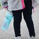 Nuby Thirsty Kids Flip It Reflex water bottle in aqua, held by a child in black pants, on a walking path.
