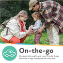 Compact Nuby travel potty urinal for girls shown with a mother and father assisting their child outdoors.