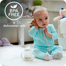 A baby in a blue onesie sits on a rug, holding a plush toy, beside a Nuk spill-proof sippy cup labeled BPA Free and dishwasher-safe.