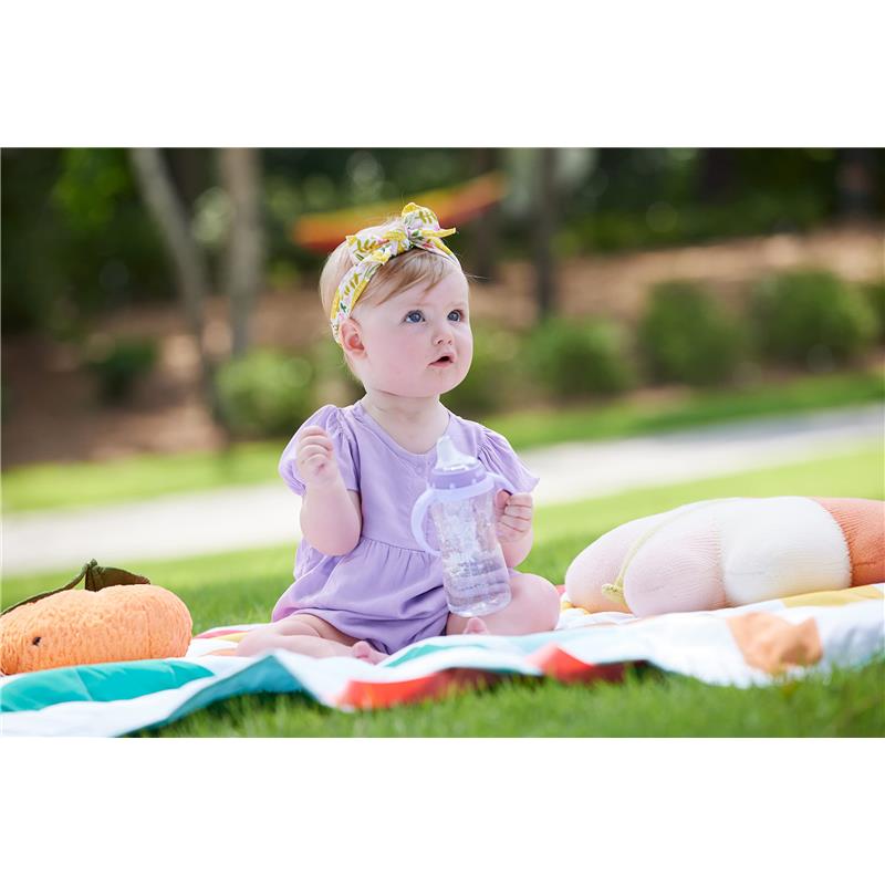 Baby sitting on a colorful blanket outdoors, holding a spill-proof Nuk Tritan sippy cup in gray with a star design.