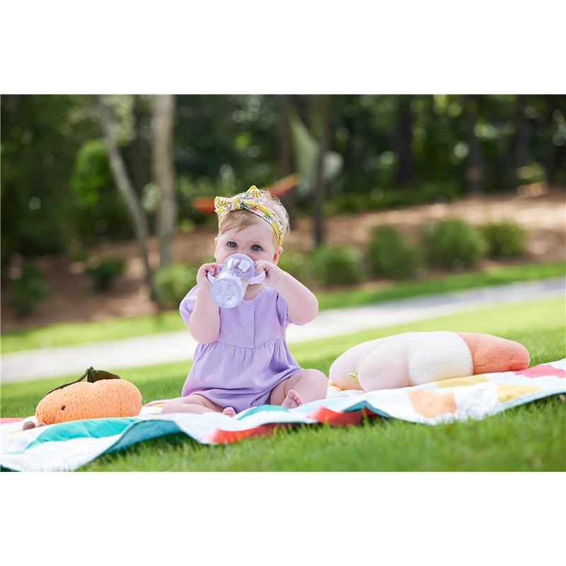 Toddler in a purple outfit sitting on a colorful blanket, holding a Tritan gray star sippy cup, surrounded by plush toys.